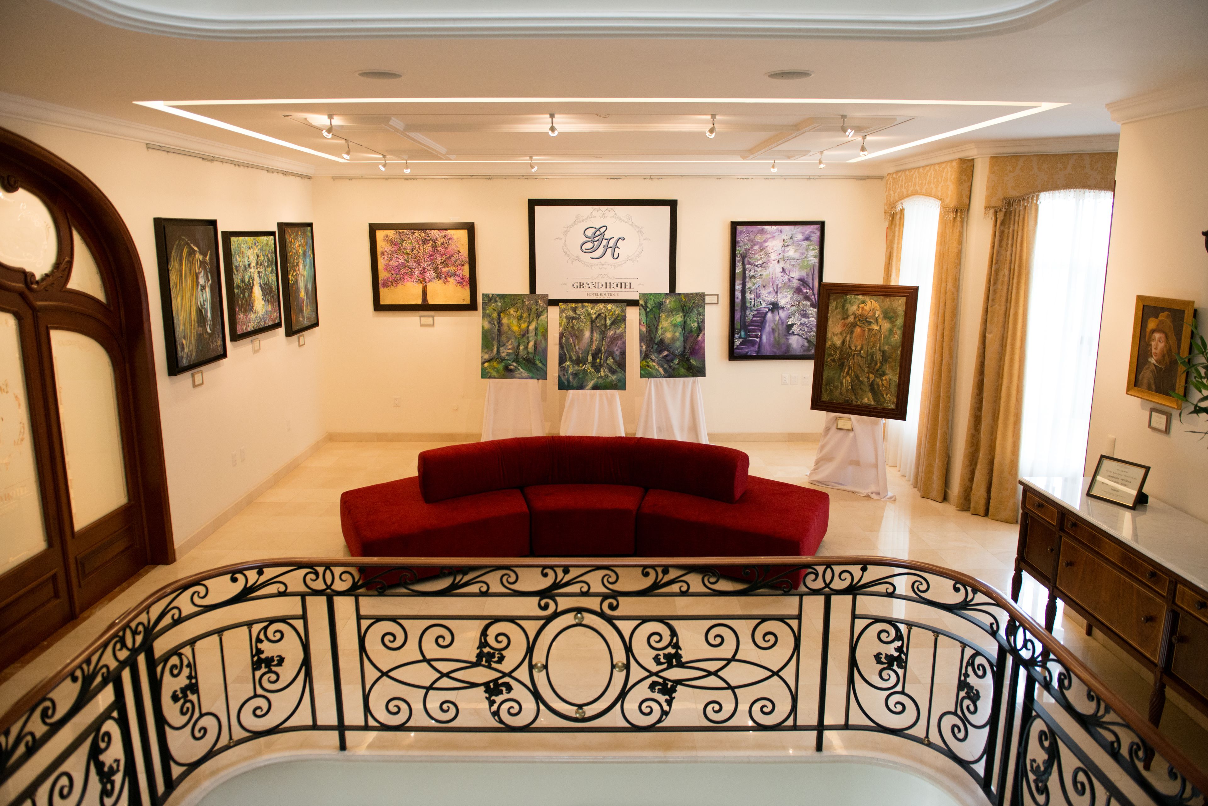 Un vestíbulo de hotel con un sofá rojo, obras de arte en las paredes y una escalera con barandillas ornamentadas.