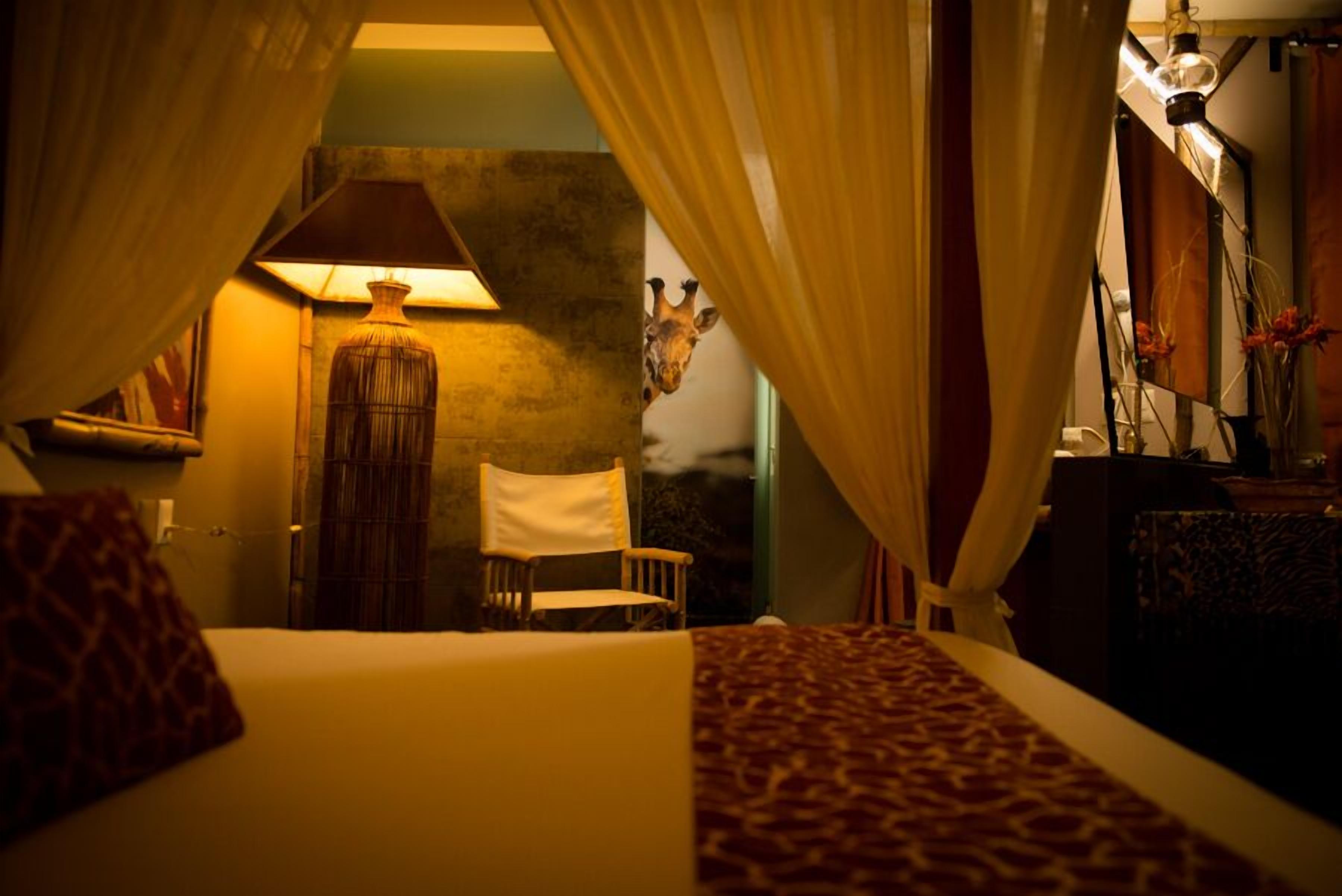 A room with a bed, a chair, a lamp, and a giraffe mural on the wall.