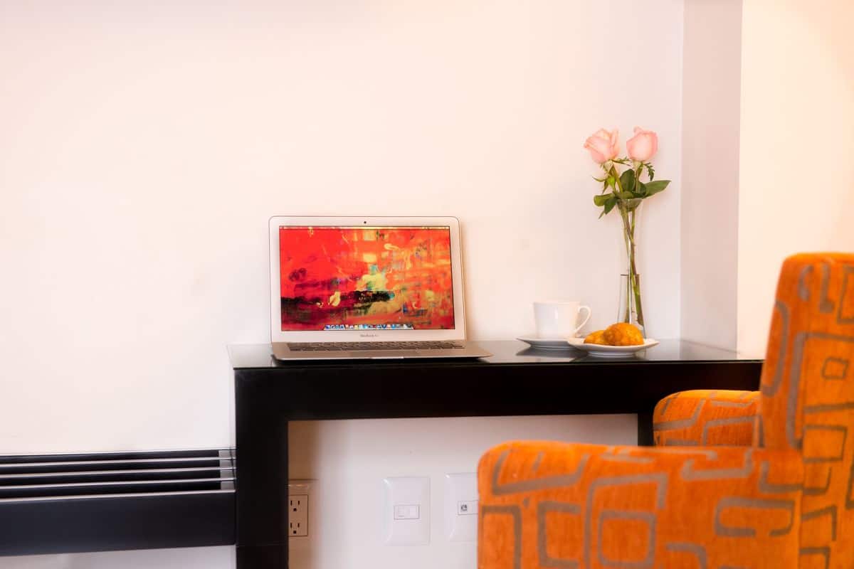 A laptop on a black desk with a vase of pink roses and a plate of food.