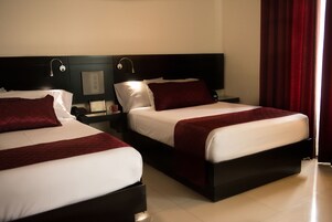 A hotel room with two beds, a nightstand with a lamp, and a red curtain.