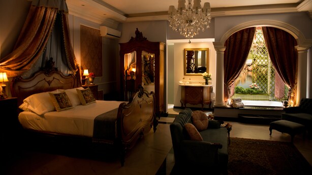 Um quarto espaçoso com uma cama grande, um espaço de estar com um sofá e vista para um jardim através de uma janela com cortinas.