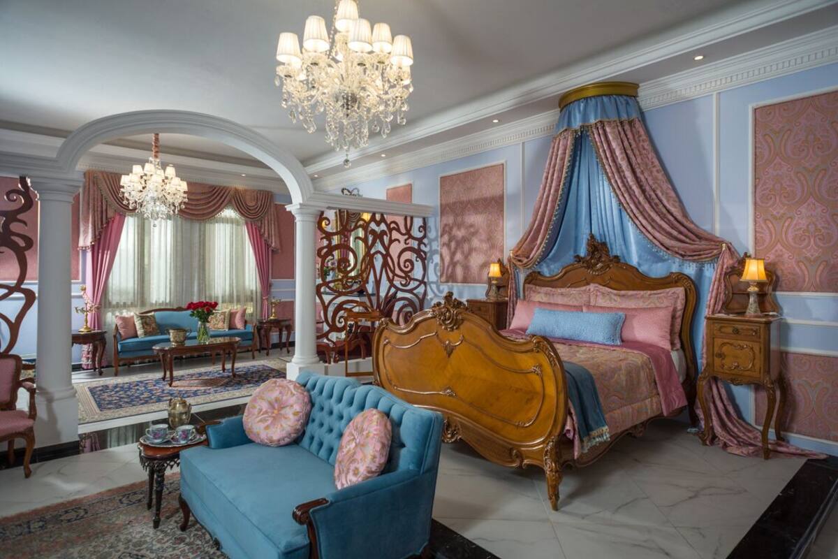 A luxurious bedroom with a large bed, ornate curtains, and a chandelier.
