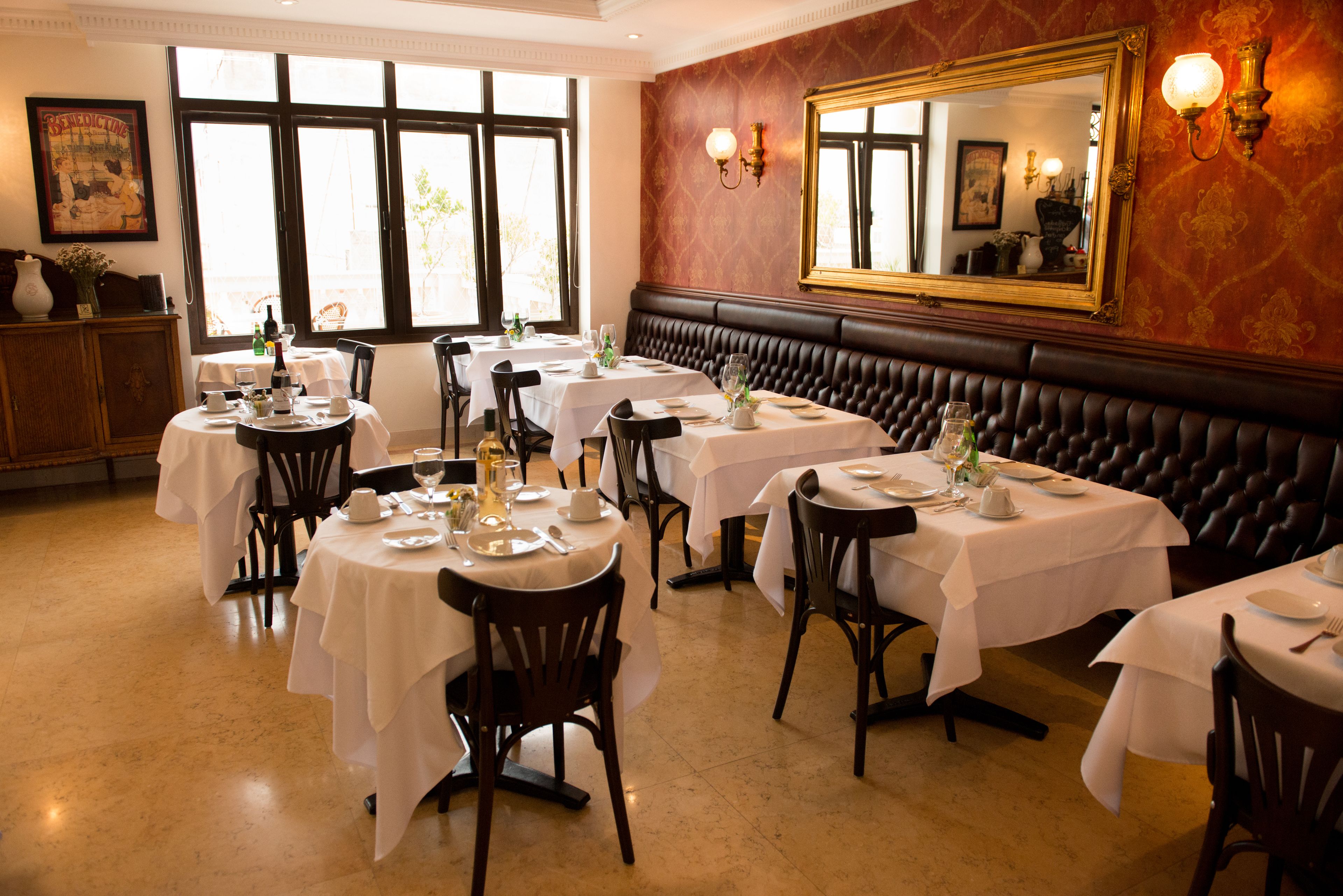 A dining area with multiple tables set for guests, a large mirror on the wall, and a view of the outdoors through large windows.