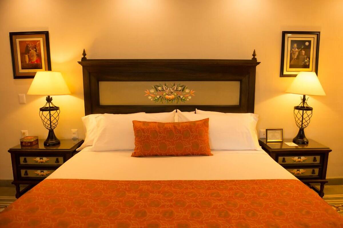 A neatly made bed with white and orange bedding, two bedside lamps, and framed artwork on the walls.