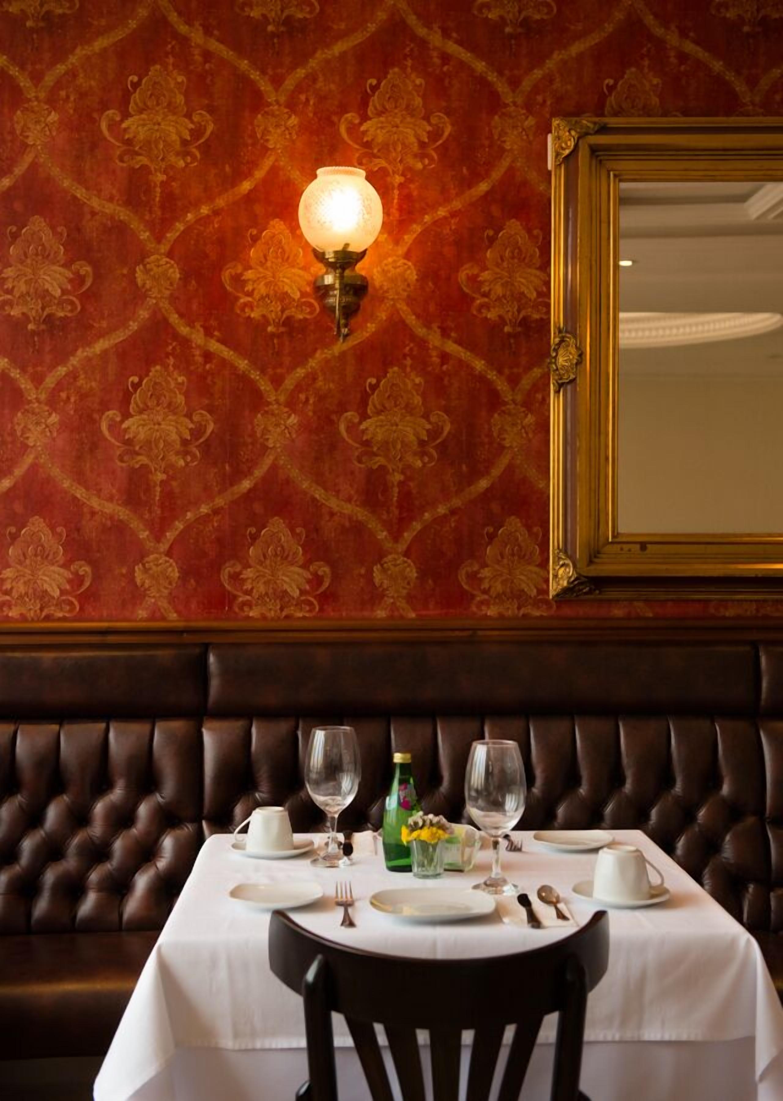 A dining area with a table set for two, a wall-mounted light, and a mirror above the table.