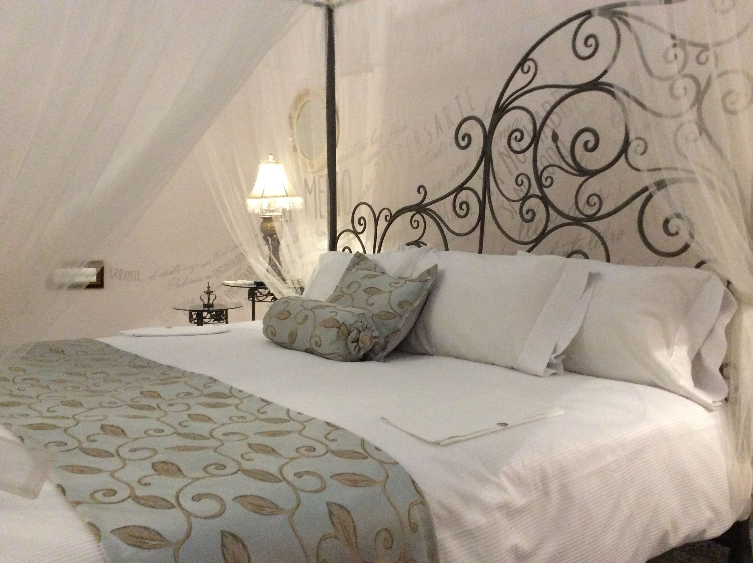 Una cama bien hecha con una colcha estampada, un cabecero decorativo y una mesita de noche con una lámpara.