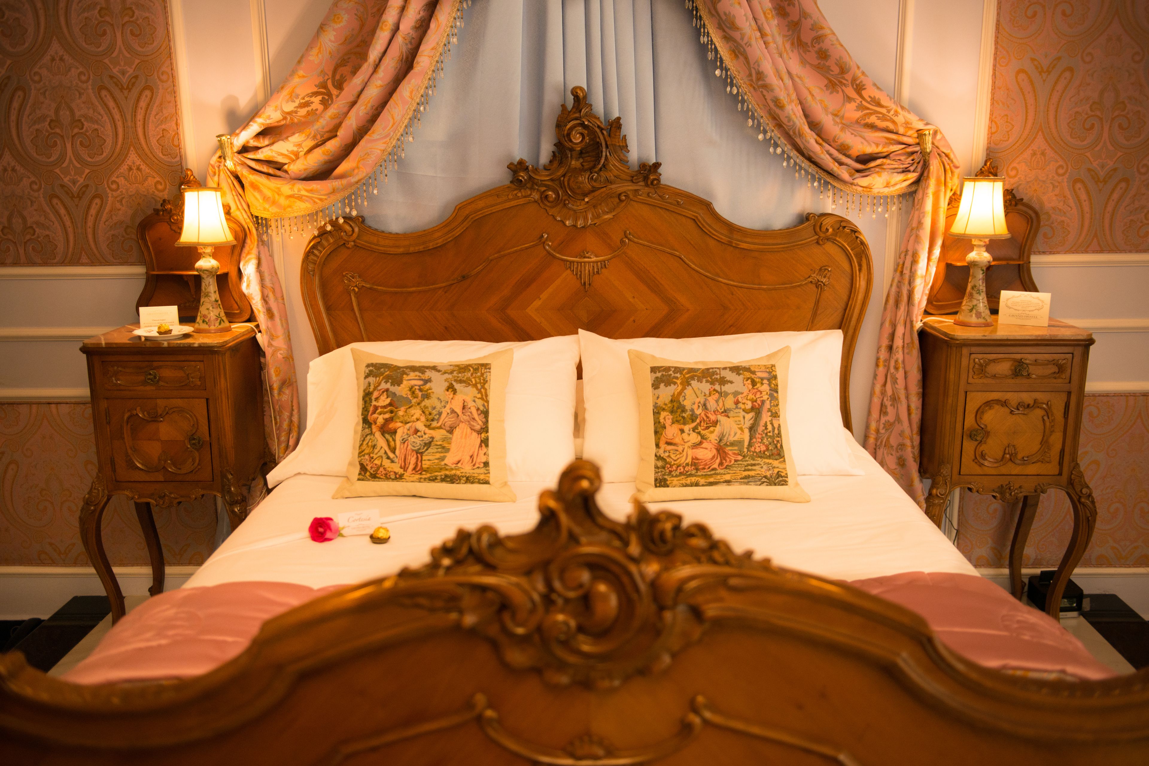 Un lit à baldaquin classique, doté d’une tête de lit et d’un pied de lit richement décorés, flanqué de deux tables de chevet avec des lampes et d’une petite table.