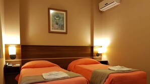 A hotel room with two beds, each with an orange bedspread and a brown blanket. There are bedside lamps, a framed picture on the wall, and an air conditioning unit above the beds. - Astro Hotel (São José dos Campos)
