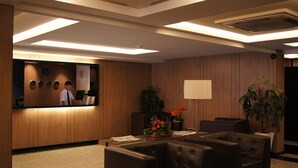 A reception area with a wooden reception desk, a clock, a plant, and leather seating. - Astro Hotel (São José dos Campos)