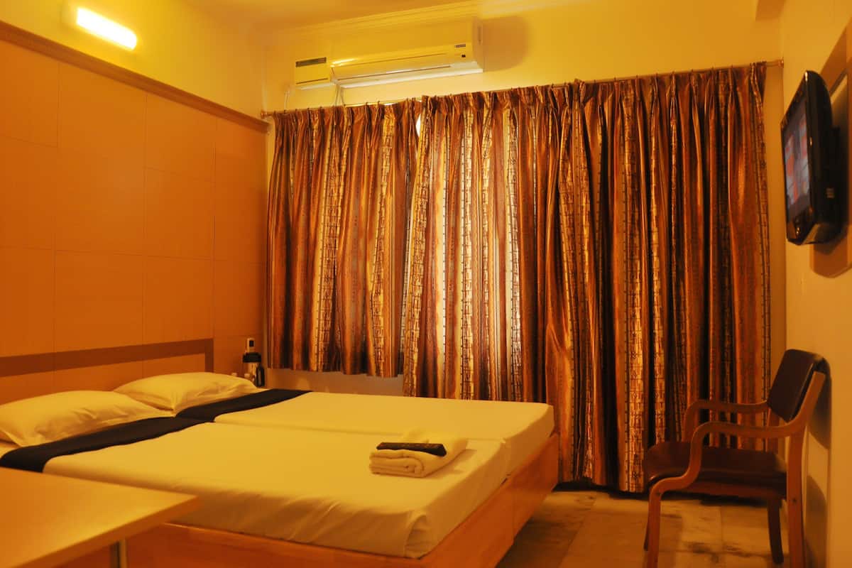 A hotel room with a bed, a chair, an air conditioning unit, and a television.