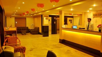 A hotel reception area with a reception desk, a waiting area with a sofa and chairs, and a reception sign.