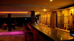 A bar area with a long counter, shelves with bottles, and a person standing at the bar. - Nayagara Hotel (Chennai)