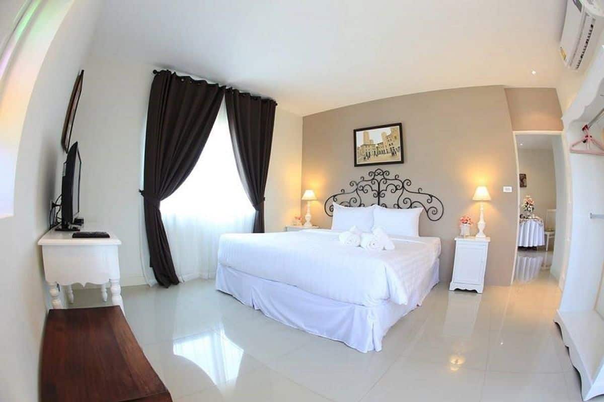 A spacious bedroom with a large bed, two bedside tables, a nightstand, and a mirror.