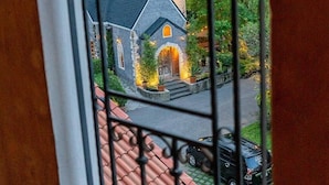 Vista a través de una ventana con reja de metal, mostrando una iglesia con un campanario alto y un edificio más pequeño con una puerta amarilla.
