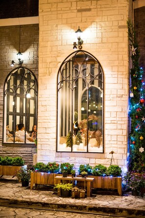 A building facade with arched windows, a brick wall, and a Christmas tree with lights. - San Pareni Hotel (Chiang Mai)