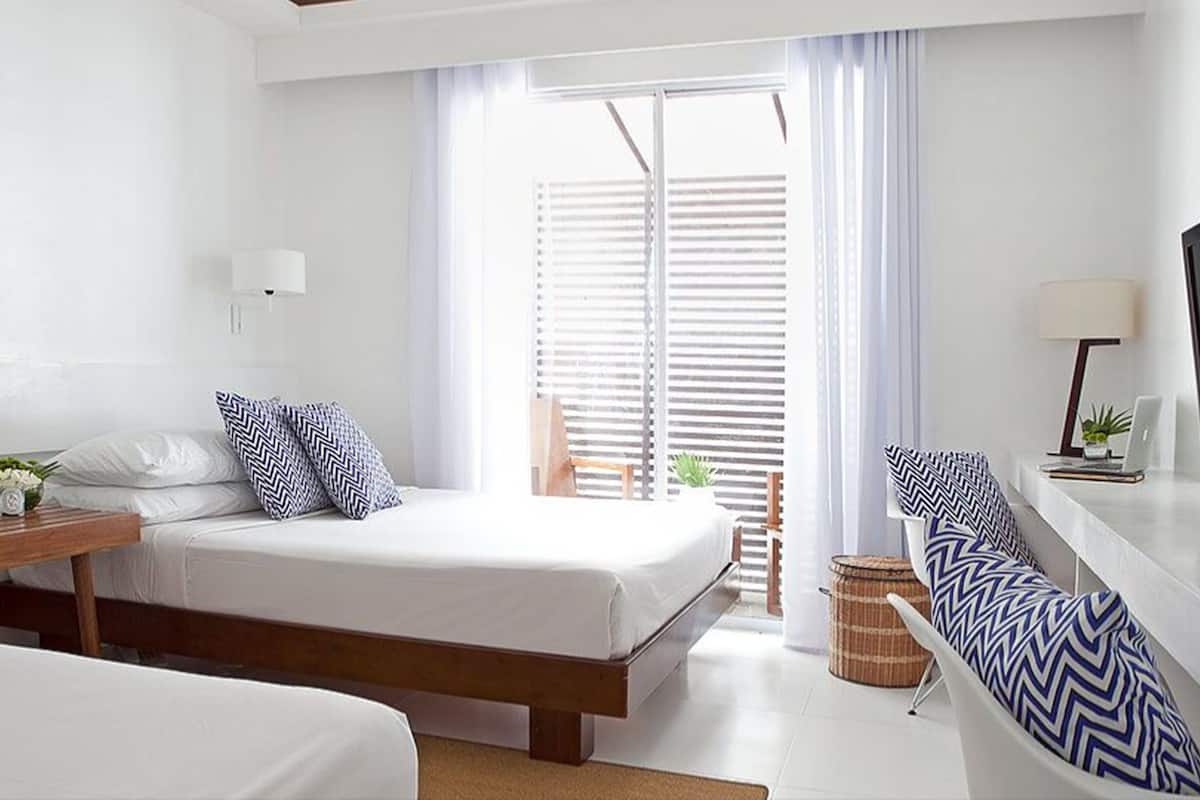 Habitación de hotel moderna con cama, mesita de noche, lámpara, televisor y vistas al exterior a través de amplias ventanas.