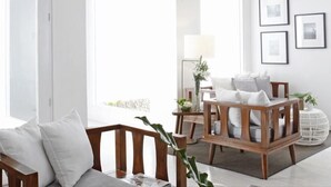 A modern living room with a wooden sofa, a wooden armchair, and a side table with a lamp. There are framed pictures on the wall and a potted plant on the side table. - Blue Marina (Boracay Island)