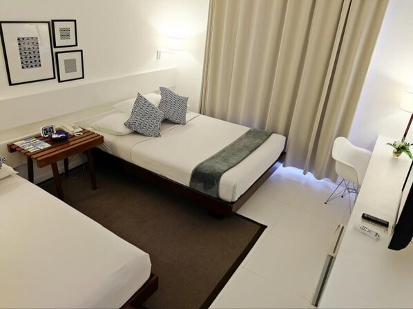 Une chambre d’hôtel avec deux lits, une table de chevet avec une lampe, une chaise et un bureau avec un ordinateur.