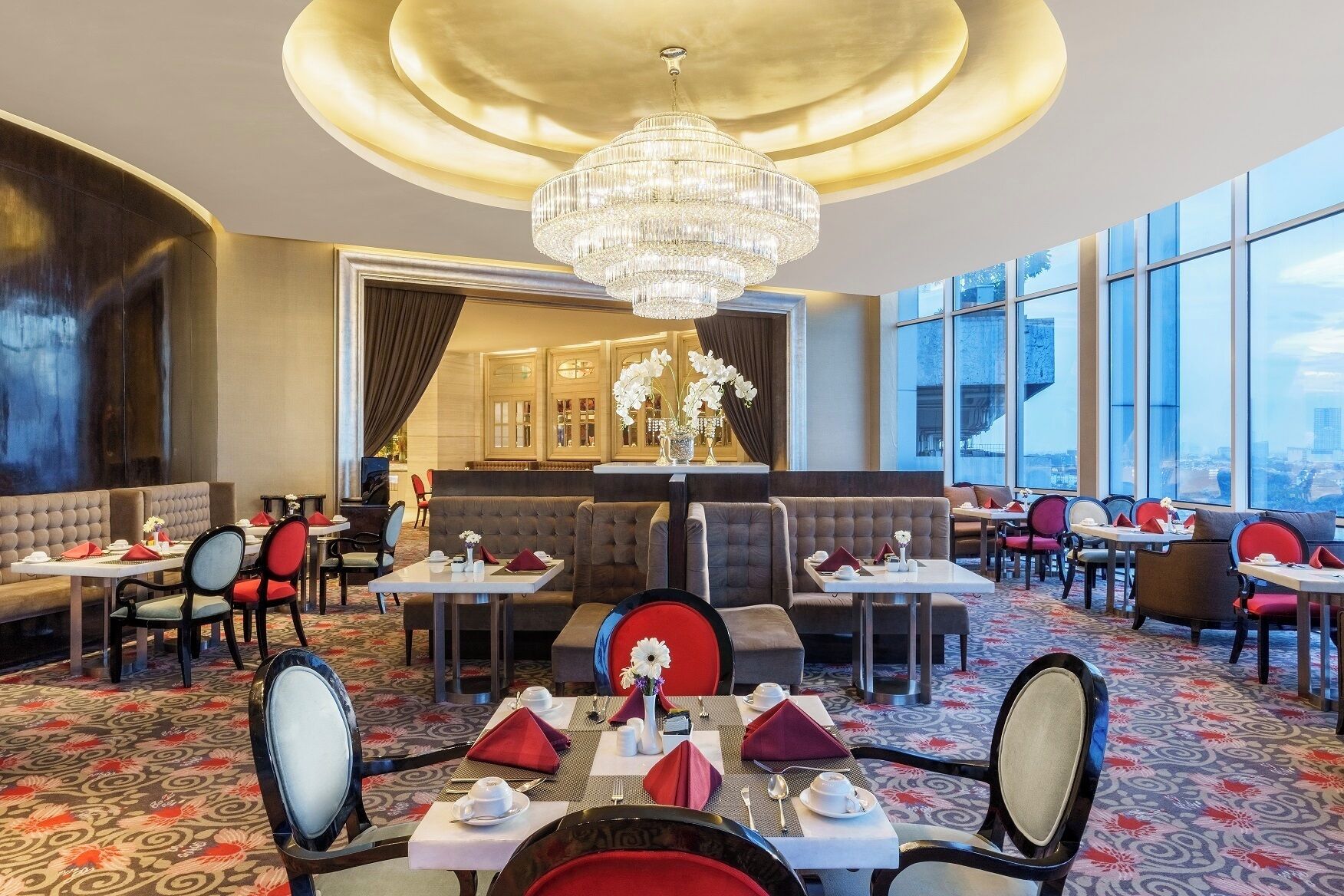 Un restaurante moderno con candelabro, disposición de mesas y amplios ventanales con vistas a la ciudad.