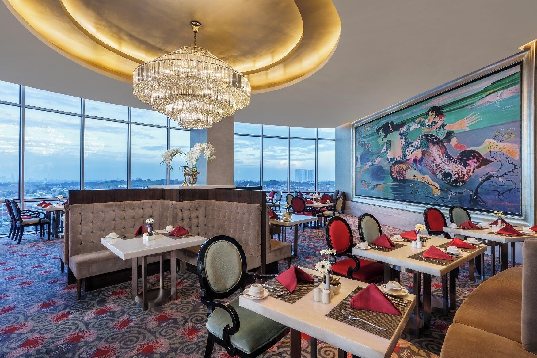 A restaurant with a view of the city, large windows, and a chandelier.