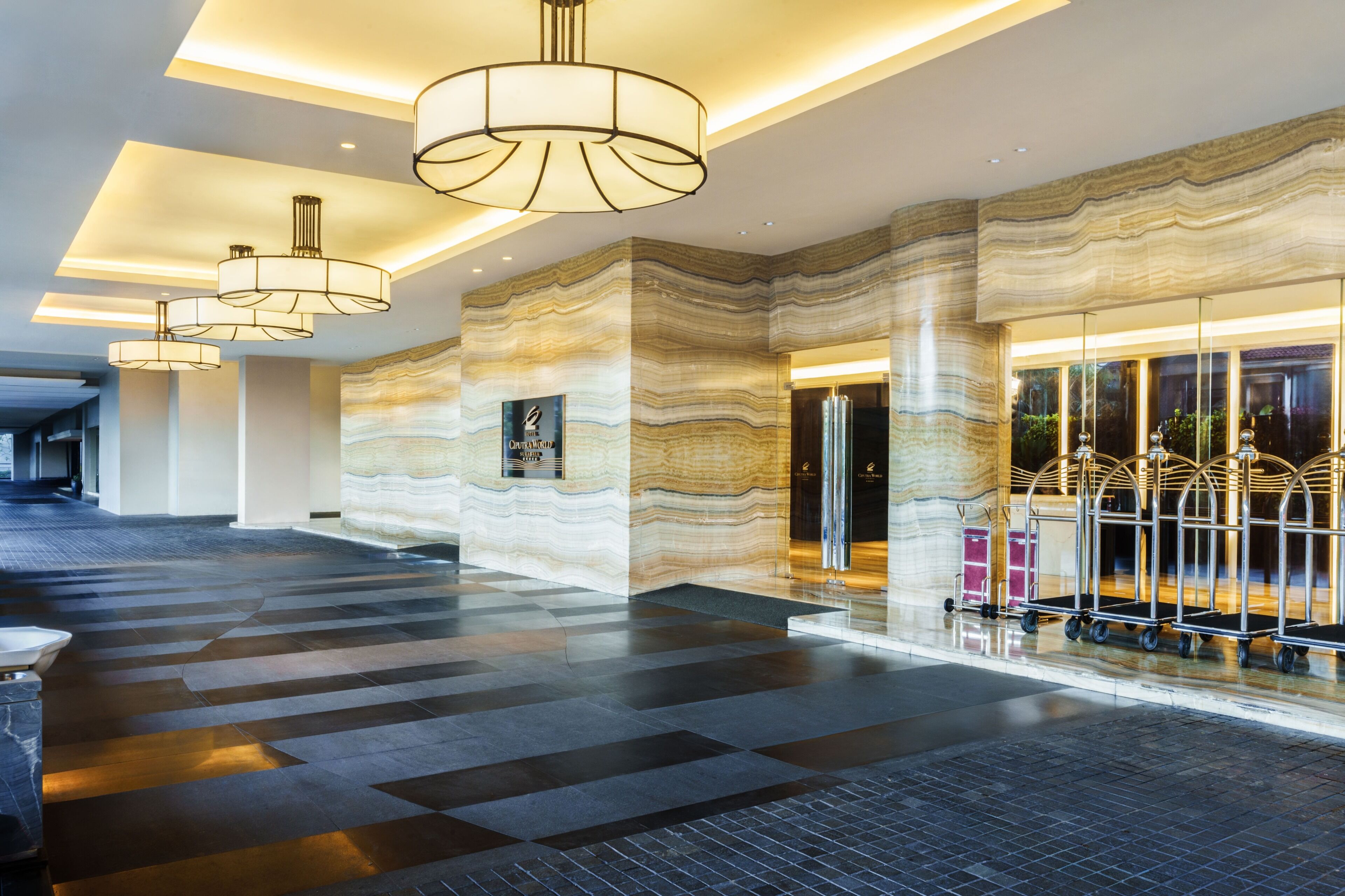 A hotel lobby with a marble wall, a reception desk, and a luggage cart.