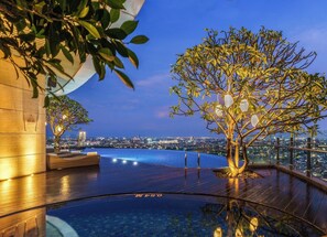 Una piscina infinita con vistas a la ciudad, un árbol y una terraza de madera.