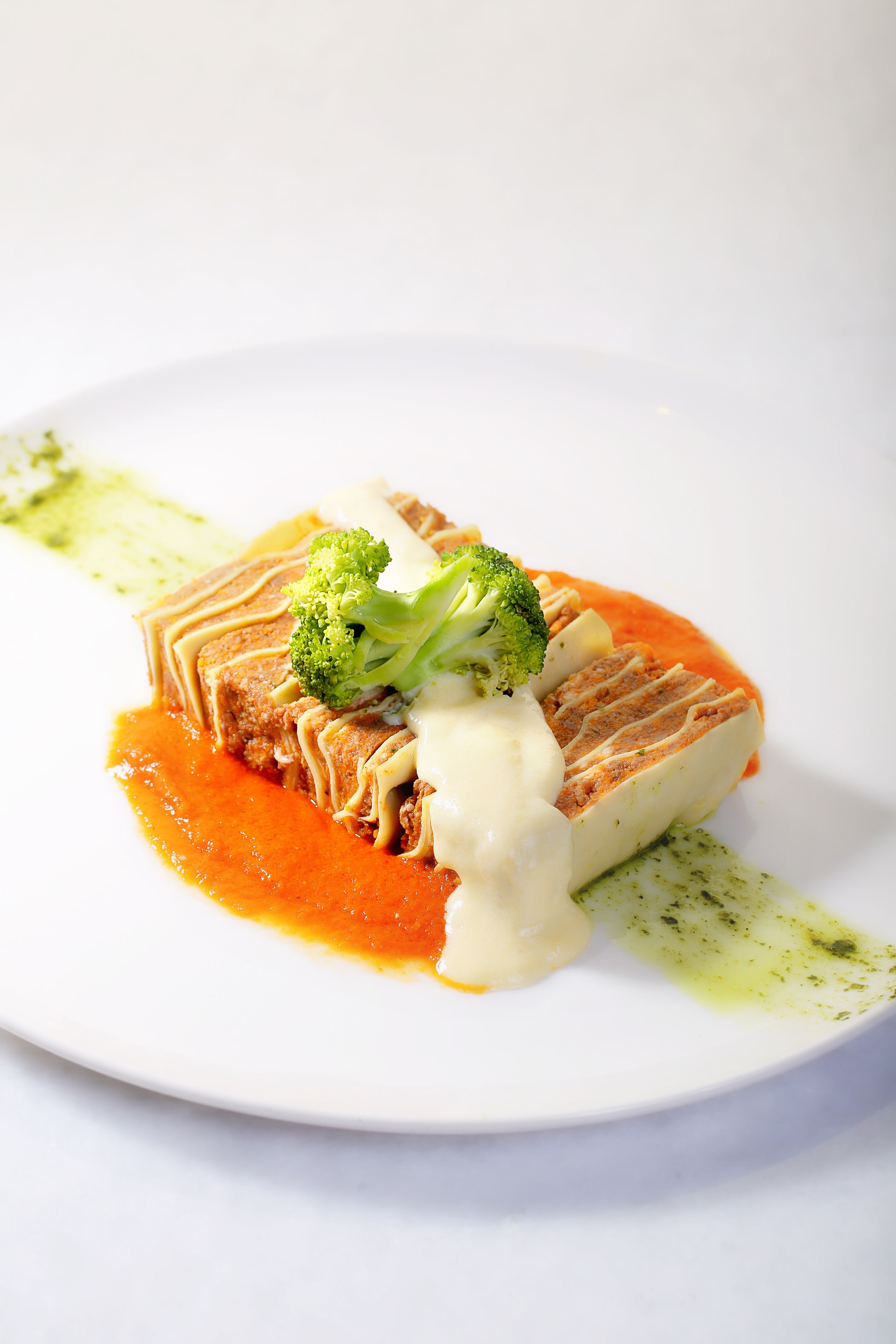 A white plate with a dish consisting of a piece of meat, broccoli, and a creamy sauce.