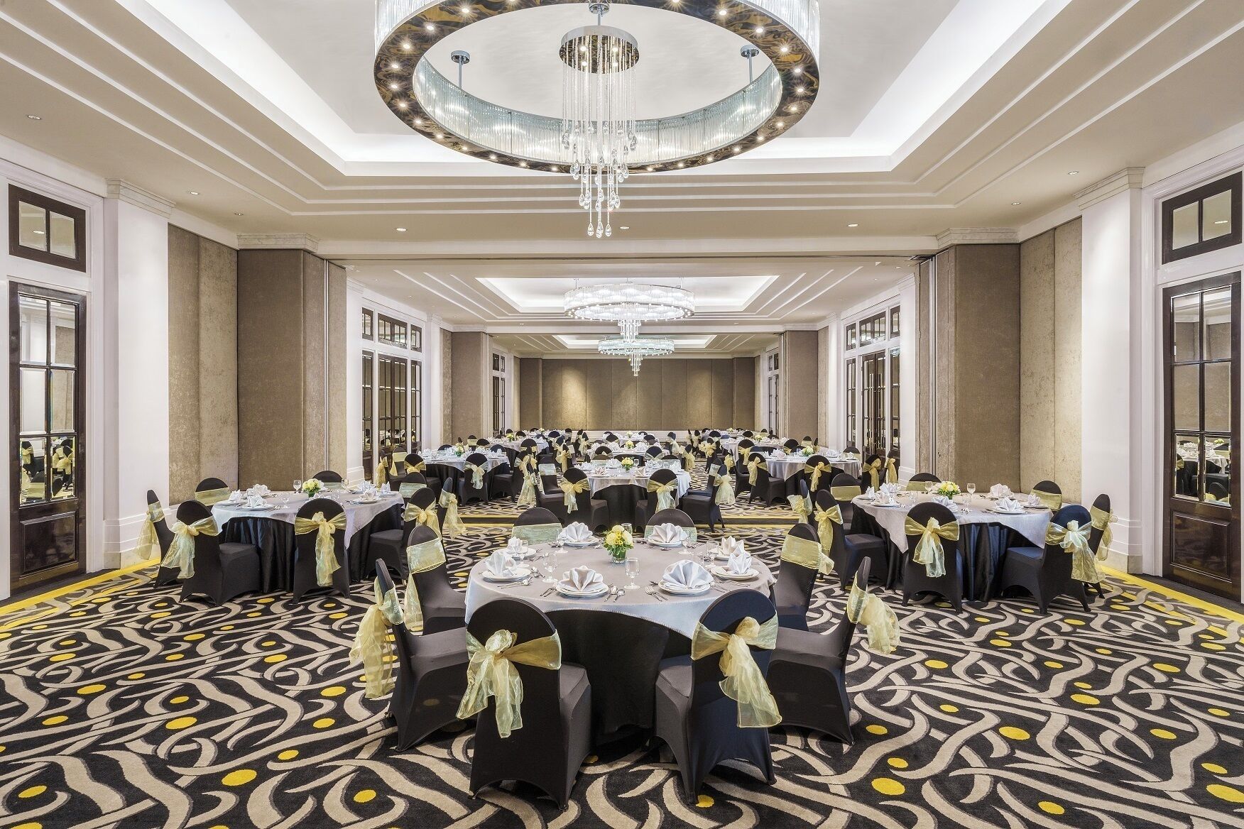 A spacious banquet hall with round tables, black chairs, and yellow sashes.