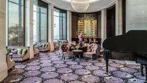 A luxurious lobby with a grand piano, plush seating, a chandelier, and a large window with a view.