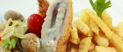 Un plato con escalope de pollo empanizado, champiñones, tomates cherry y papas fritas.
