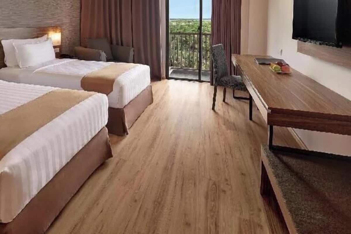 Habitación de hotel con dos camas, un escritorio, una silla, un televisor y un balcón con vistas.