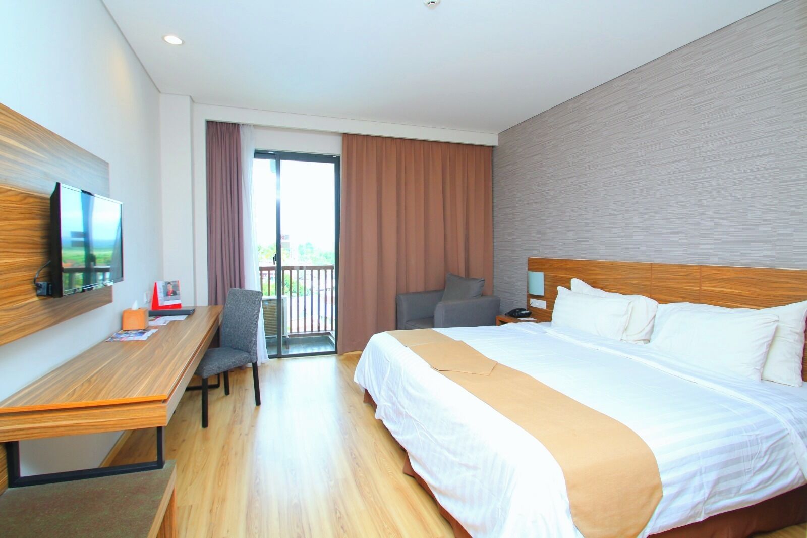 Une chambre d’hôtel avec un lit, un bureau, une chaise et un téléviseur fixé au mur.