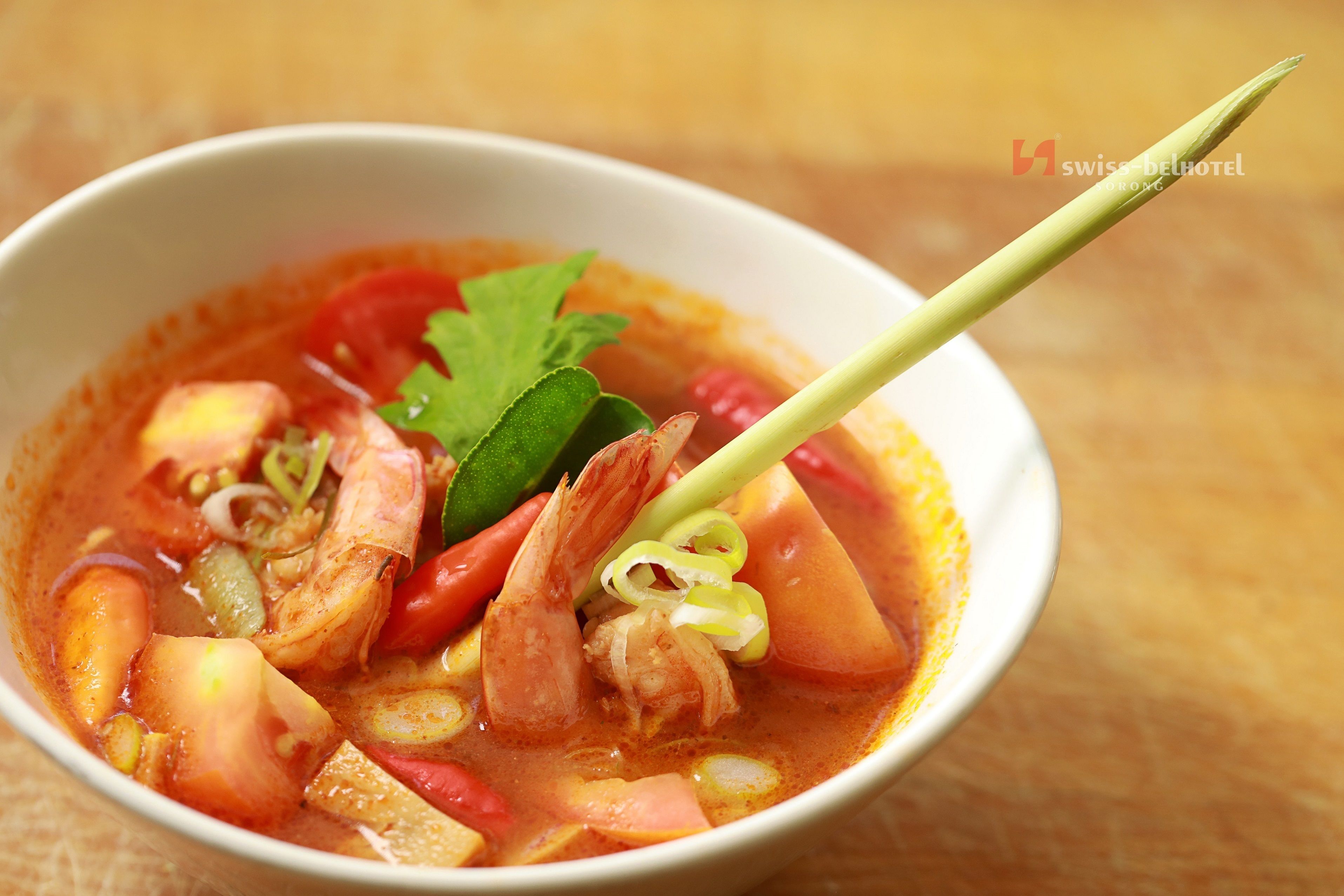 A bowl of soup with various vegetables and shrimp, garnished with a leaf and a green stalk.