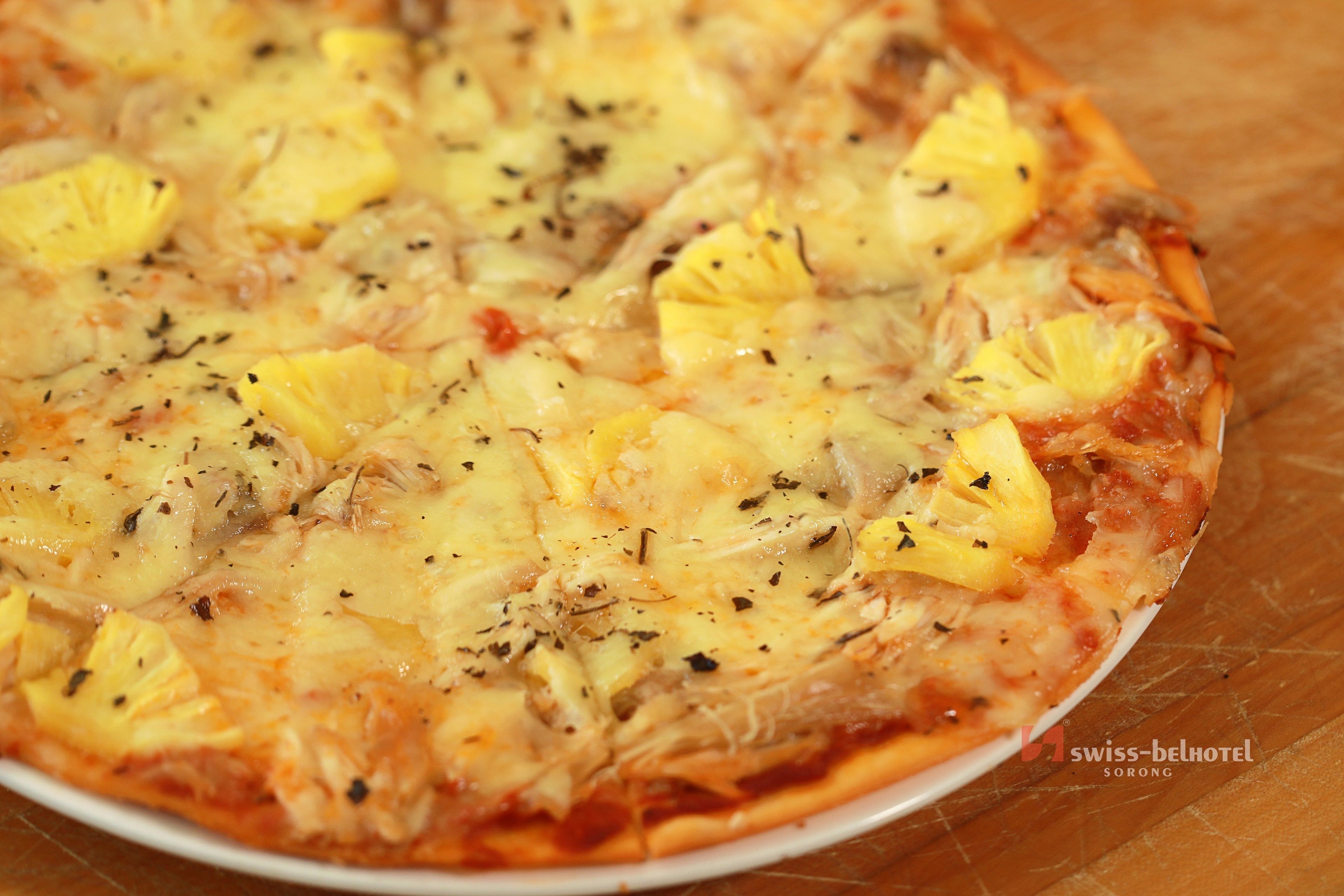 A pizza with pineapple and herbs on a white plate.