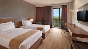 Ein Hotelzimmer mit zwei Betten, einem Schreibtisch, einem Stuhl, einem Fernseher und einem Balkon mit Aussicht.