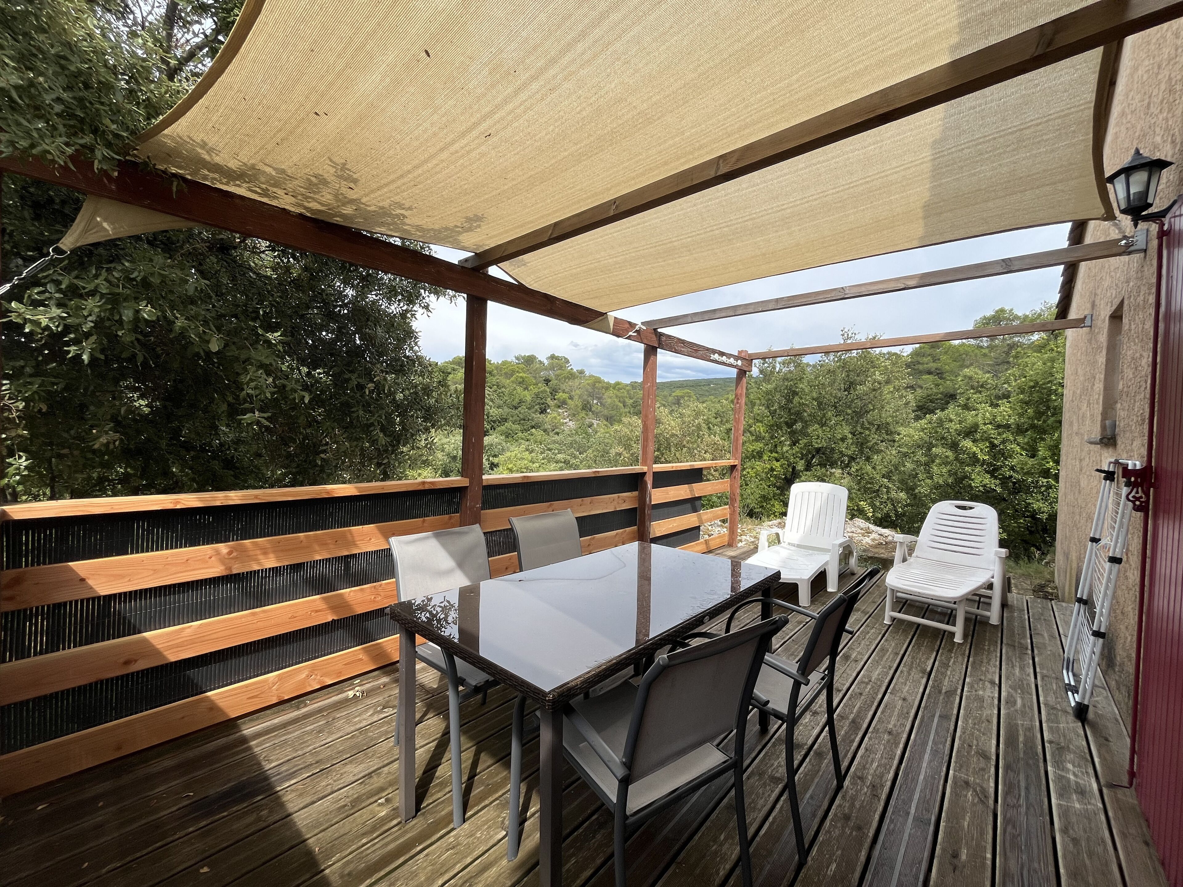 Un espacio de estar al aire libre con techo, que cuenta con una mesa y sillas, rodeado de barandas de madera y vistas a follaje.