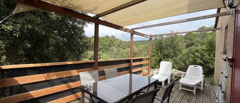 Un espacio de estar al aire libre con techo, que cuenta con una mesa y sillas, rodeado de barandas de madera y vistas a follaje.