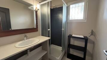 Une salle de bain moderne avec un lavabo blanc, une douche à parois de verre et une petite étagère noire.