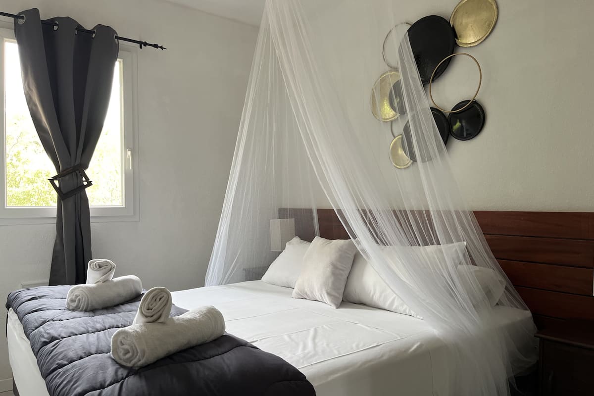 A neatly made bed with white linens, a grey quilt, and a canopy.
