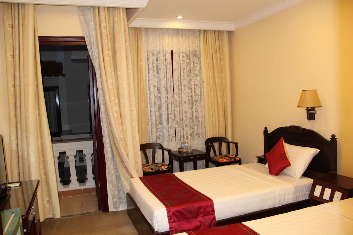 Une chambre d’hôtel avec deux lits, une fenêtre avec des rideaux, une table de chevet avec une lampe et une chaise.