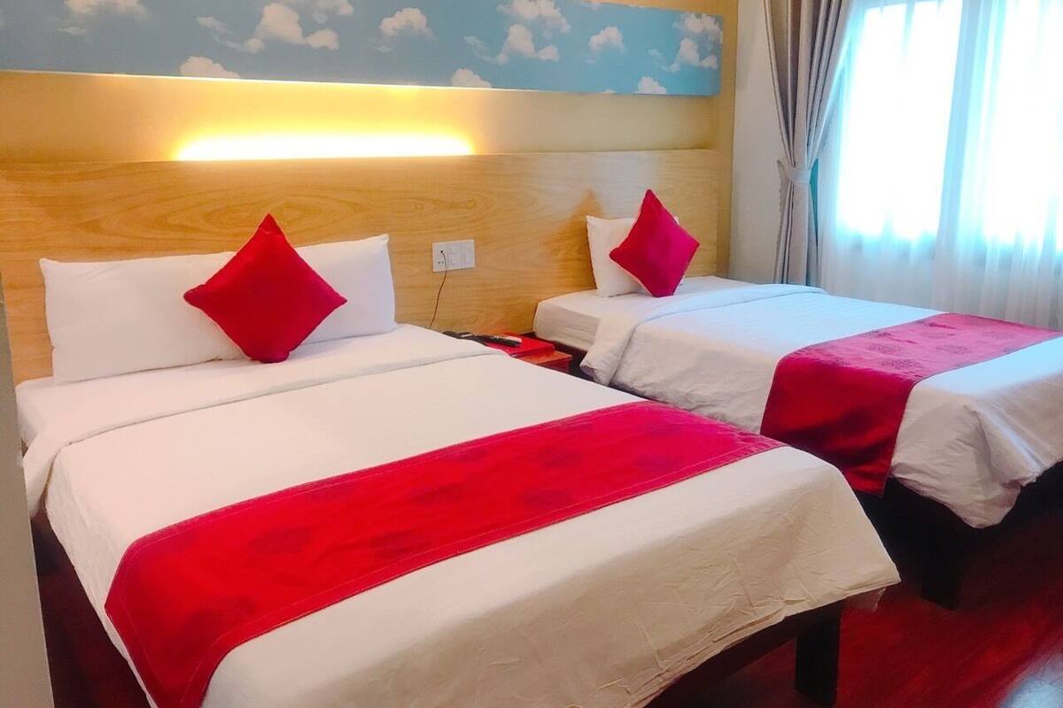 Deux lits avec une literie blanche et des touches de rouge, une tête de lit en bois et une fresque murale représentant des nuages.
