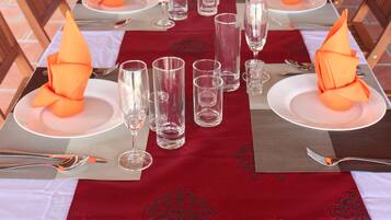Una larga mesa de comedor dispuesta con servilletas anaranjadas, copas de cristal transparentes y platos blancos.