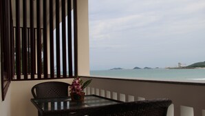 Un balcón con mobiliario de mimbre y una mesa de vidrio, con vistas a un mar tranquilo y a islas lejanas.