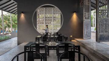 Un área de comedor al aire libre con un ventanal circular, sillas de metal negro y piso de baldosas.