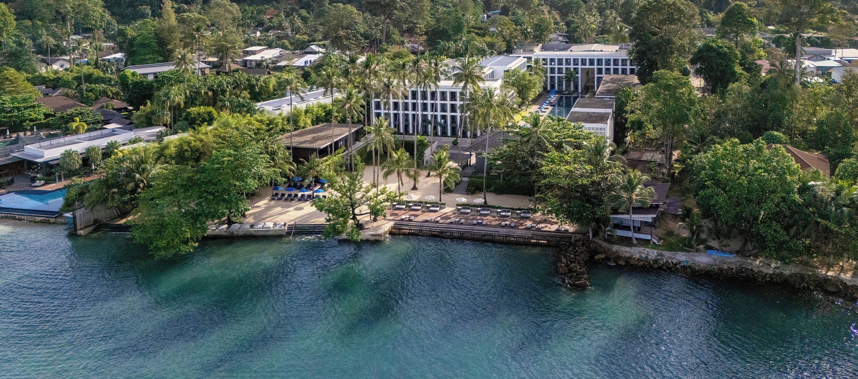 An aerial view of a resort with a pool area, multiple buildings, and lush greenery.