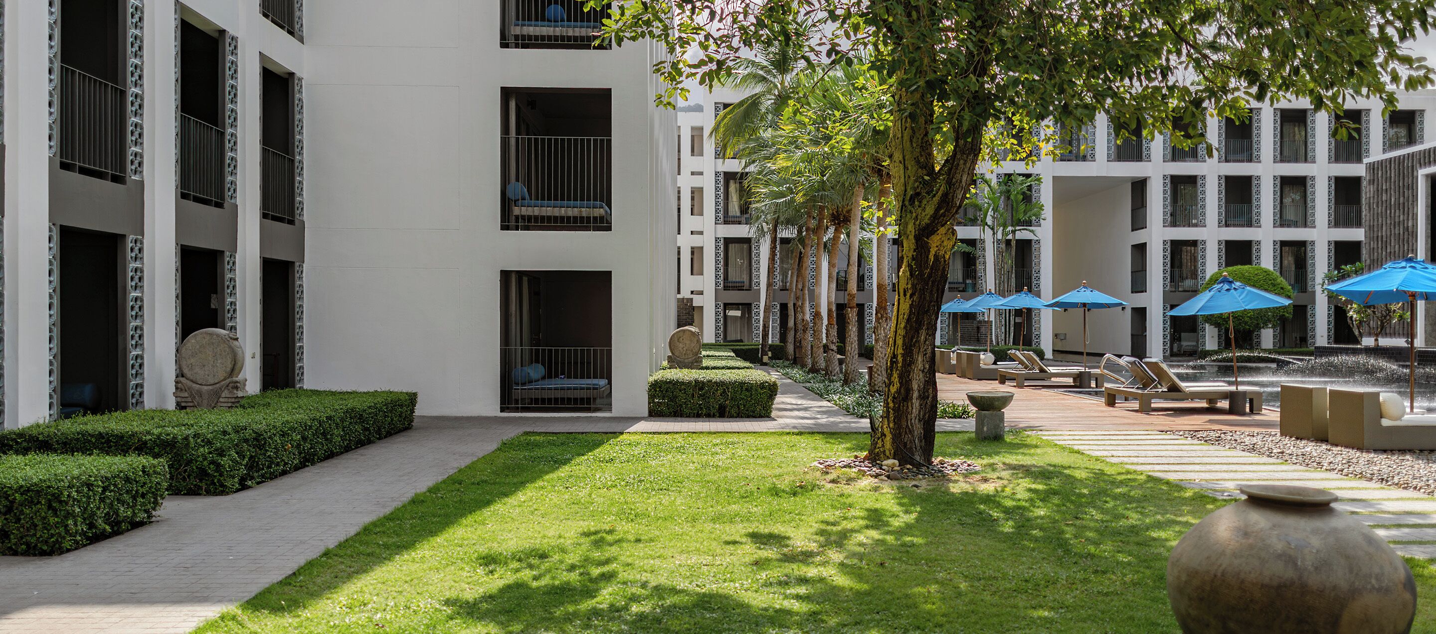 Une cour intérieure avec un chemin, des espaces aménagés pour s’asseoir et un élément décoratif aquatique.