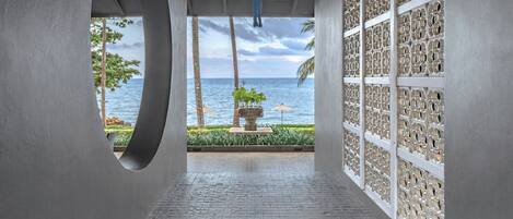 A corridor with a view of the sea, palm trees, and a stone statue.