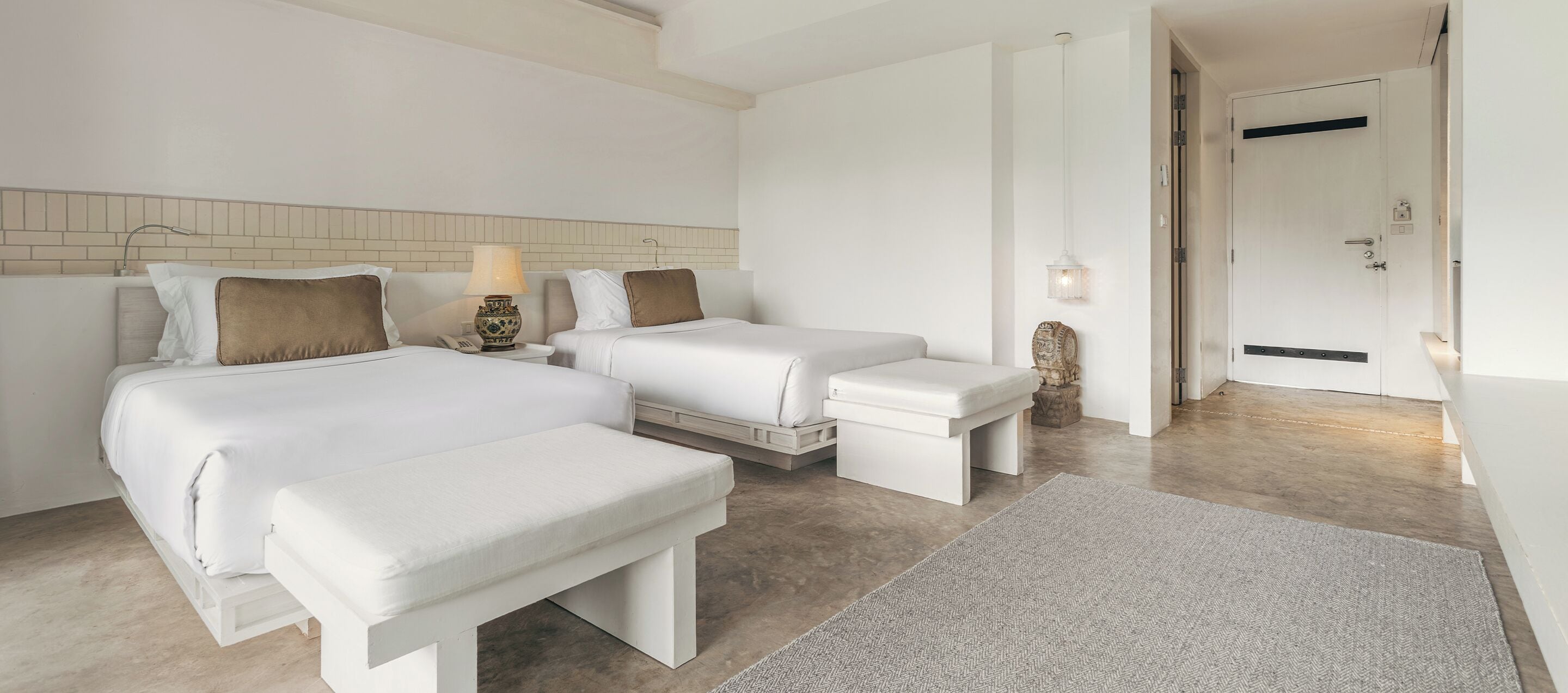 Habitación de hotel con dos camas, un banco, una lámpara y una escultura de piedra.