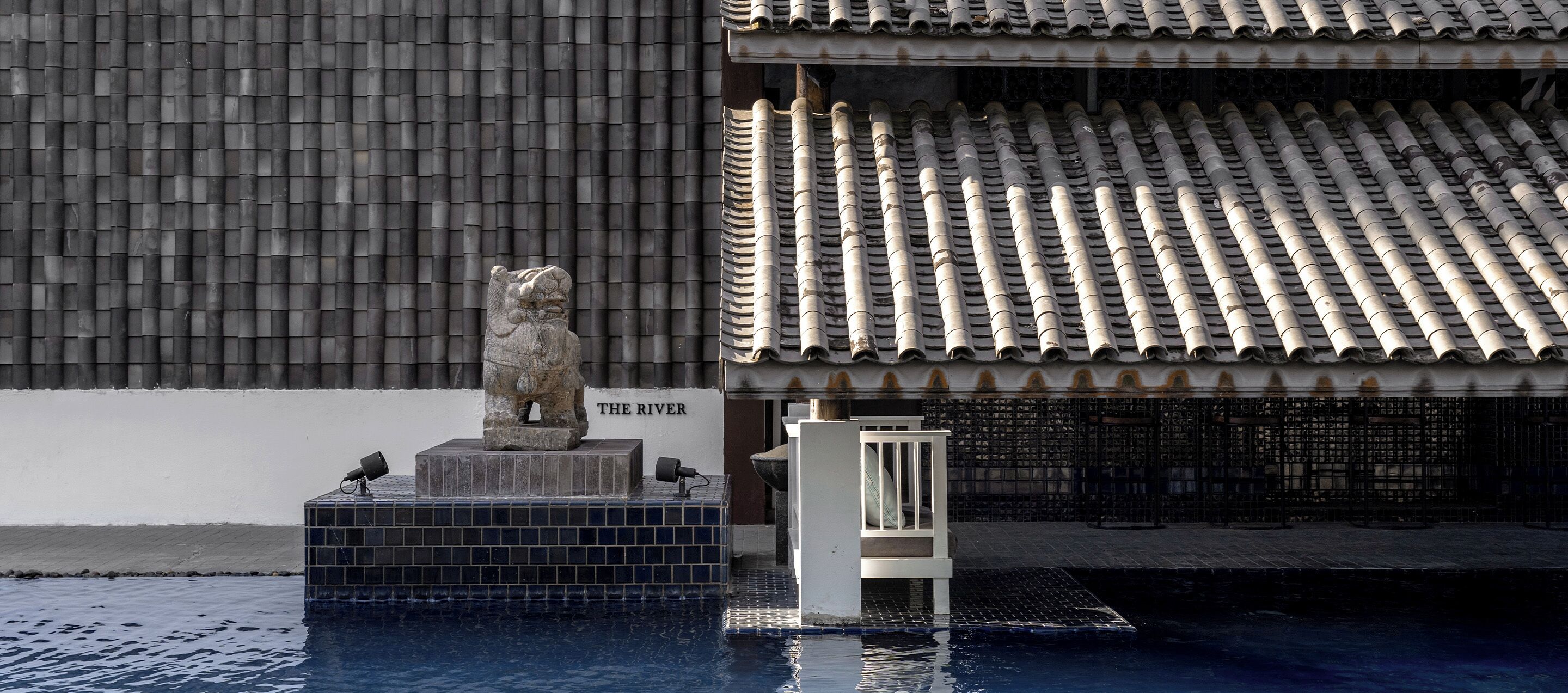 Una estatua de león de piedra en un estanque, un tejado de azulejos y un edificio con un letrero que dice "THE RIVER".