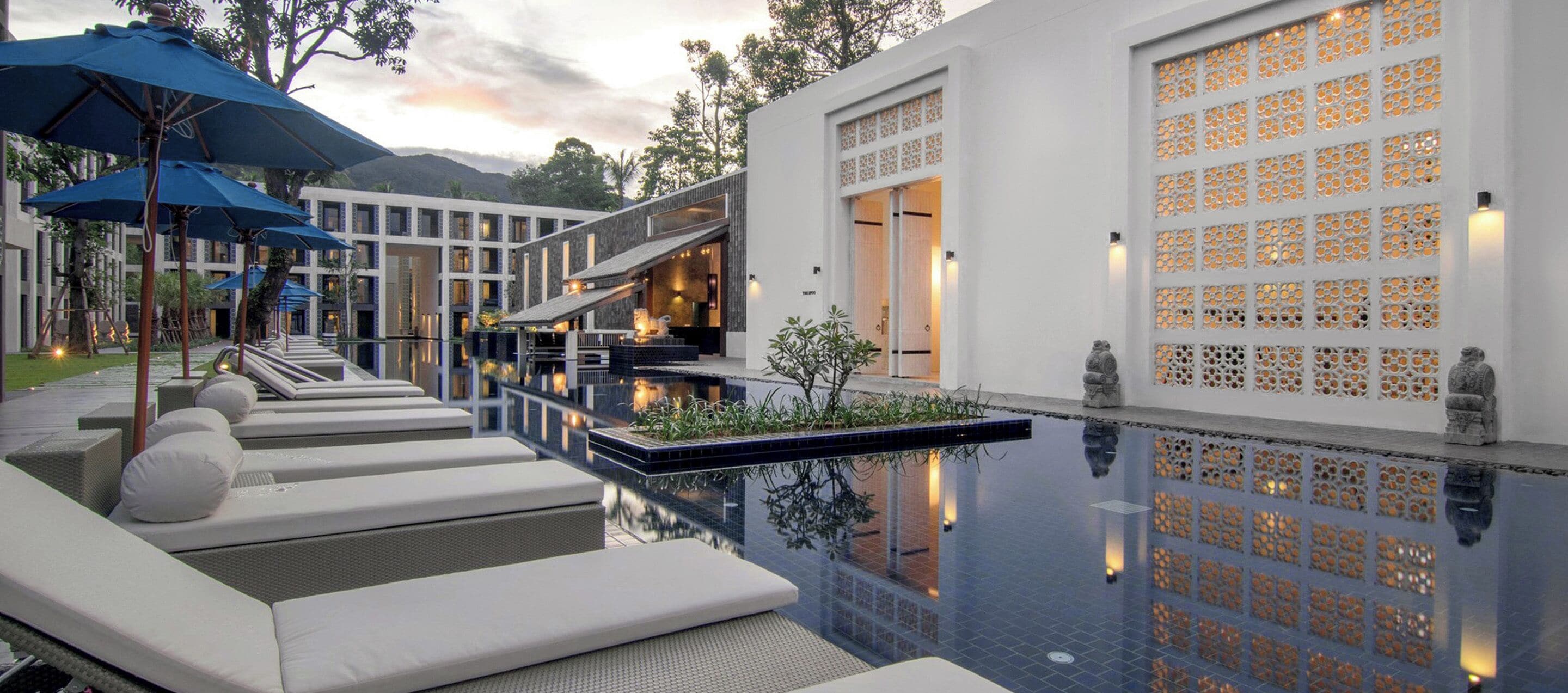 A modern hotel with a swimming pool, lounge chairs, and a decorative wall with a lattice design.